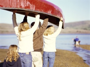 Photo of women holding a canoe overhead, walking to the water