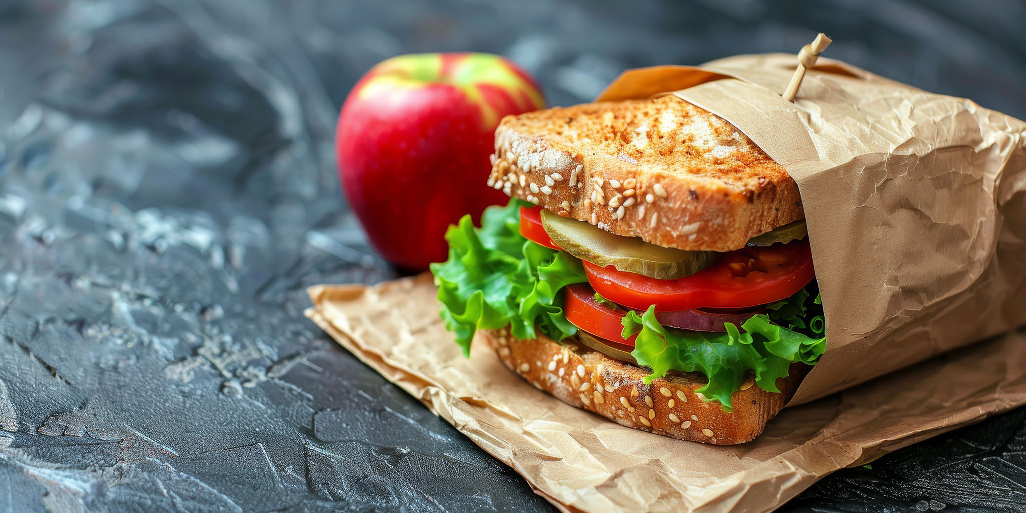 Sandwich with vegetables and an apple as a side.