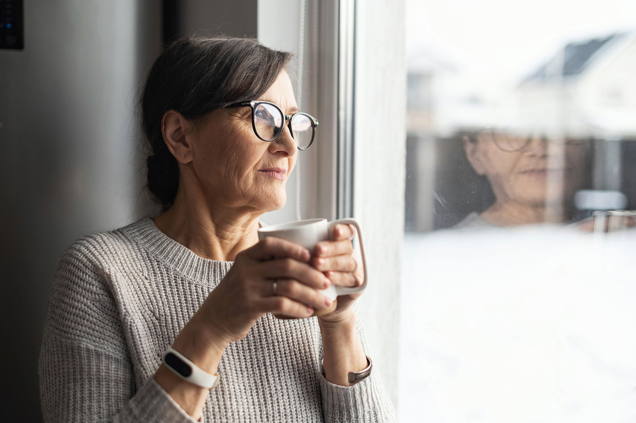 Woman holding mug and looking out window.