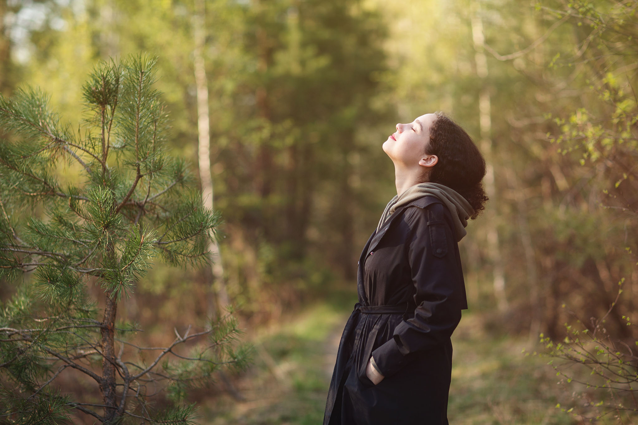 Woman standing in the woods taking a deep breath.
