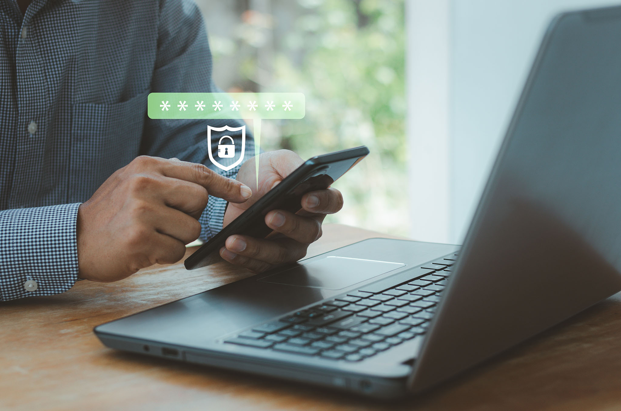 Man sitting by laptop and holding cell phone.