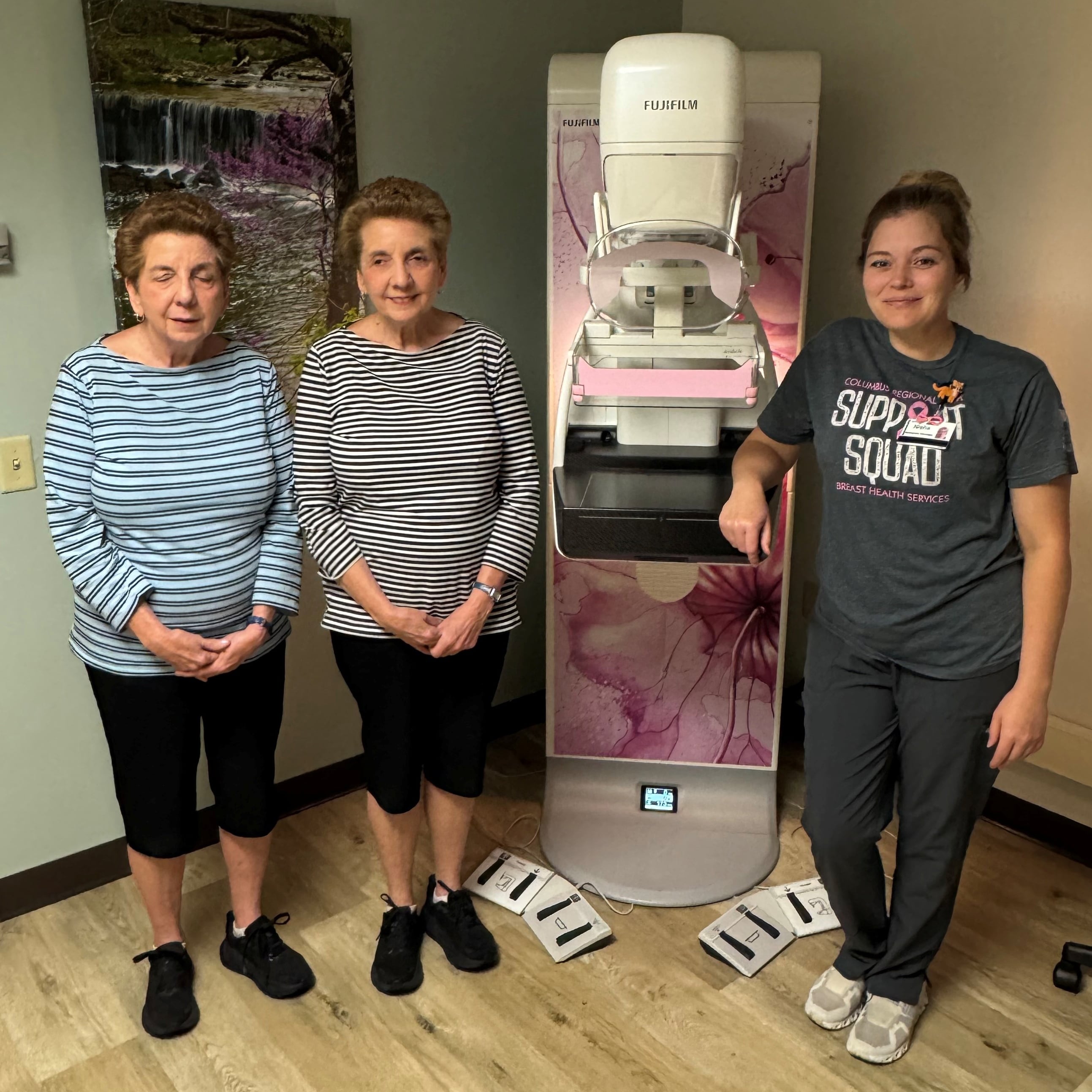Two older women and a younger woman stand next to a mammography unit