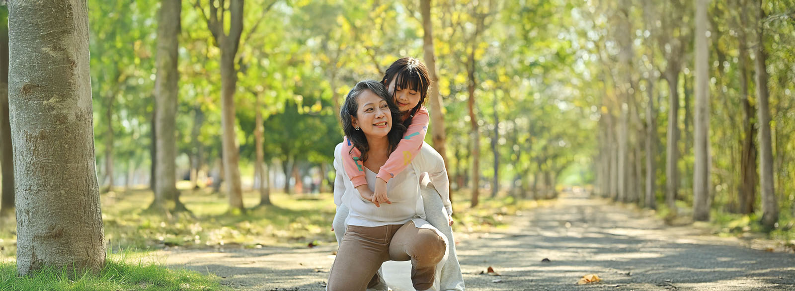 Happy middle age grandmother and grandchild walking in public park surrounded by green trees at sunlight morning.