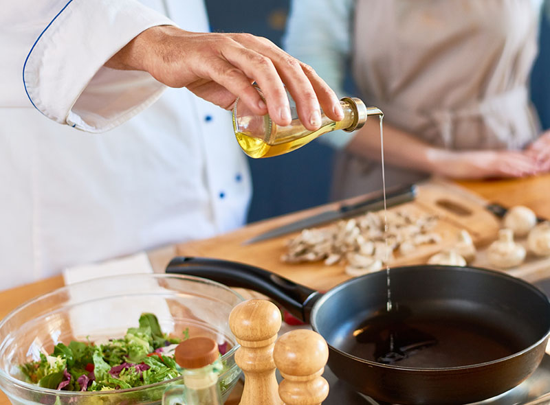Closeup of chef pouring oil into a skillet.