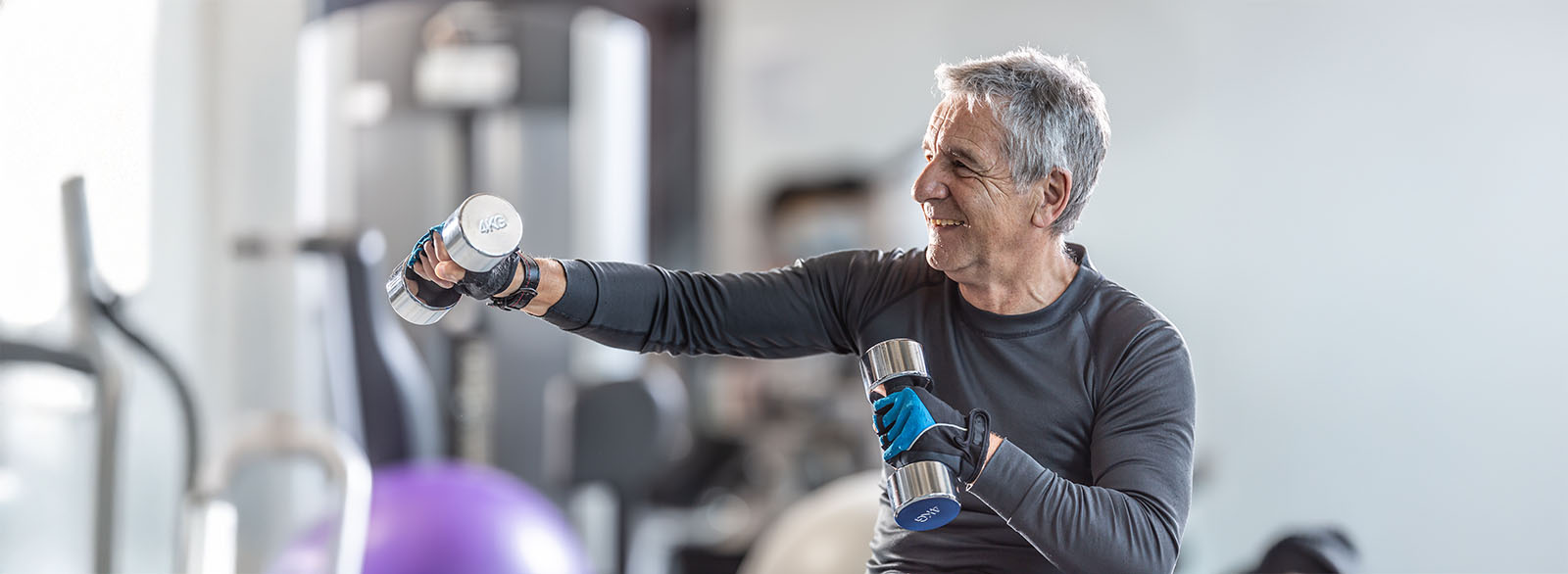Older man working out with dumbbells inside the gym, smiling.