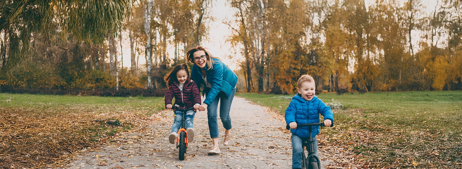 Mother playing with her daughter and son riding bicycles in a park.