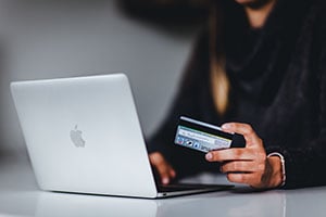 Hand holding credit card beside laptop computer.