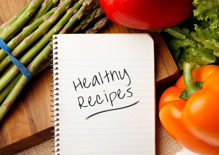 Healthy recipes notepad surrounded by vegetables and a cutting board.