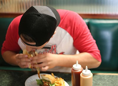 Man in baseball cap eating hamburger like a savage.