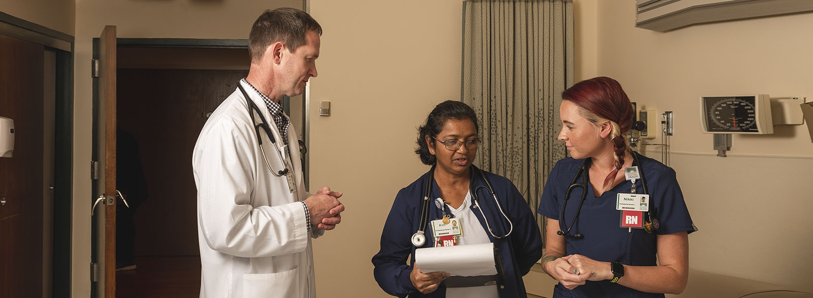 Physician preceptor speaking with nurses in a patient room.