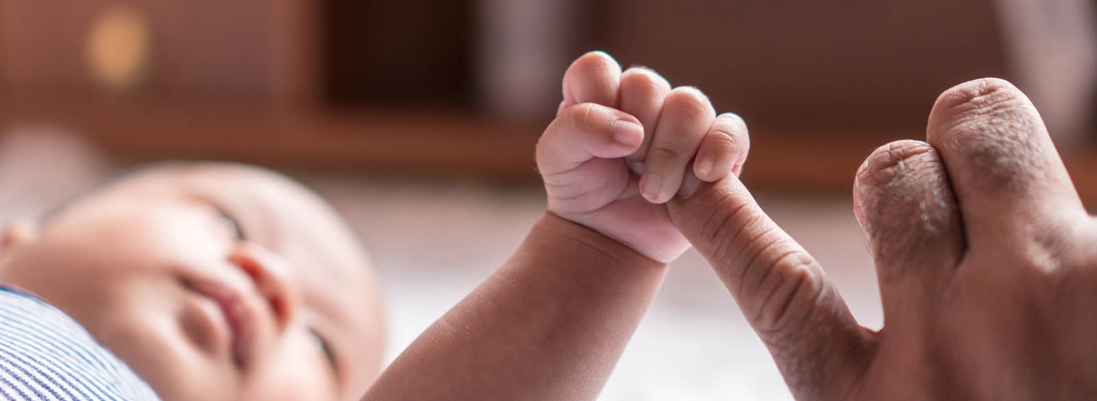 Infant boy whose hand is grasping the pinky finger of an adult.