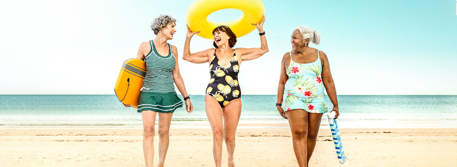 Three women walking together on a beach laughing.