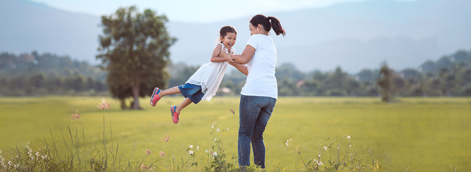 Woman spinning her daughter in a meadow.