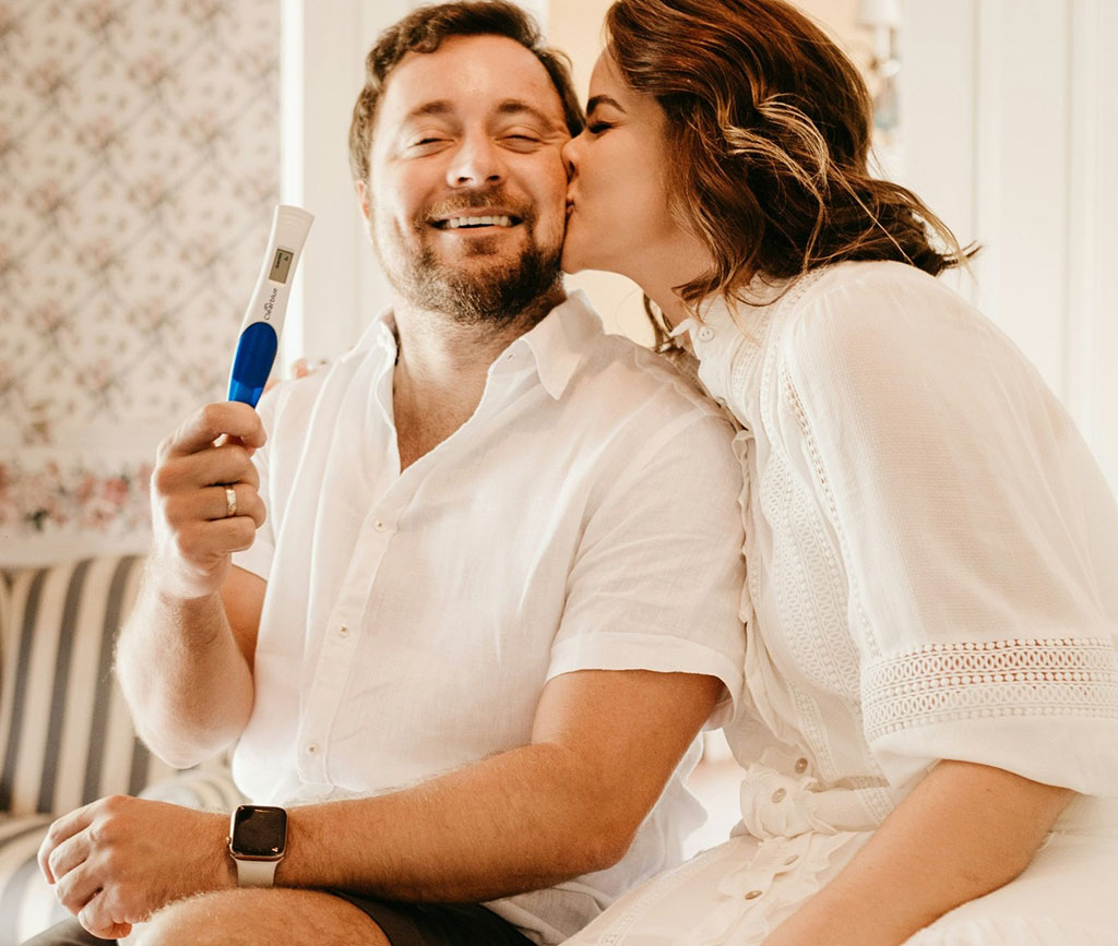 Woman kissing man holding a pregnancy test kit.